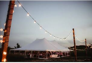 High-peak pole tent wedding at night with glowing string lights in Lake Orion, MI by Knights Tent & Party Rental